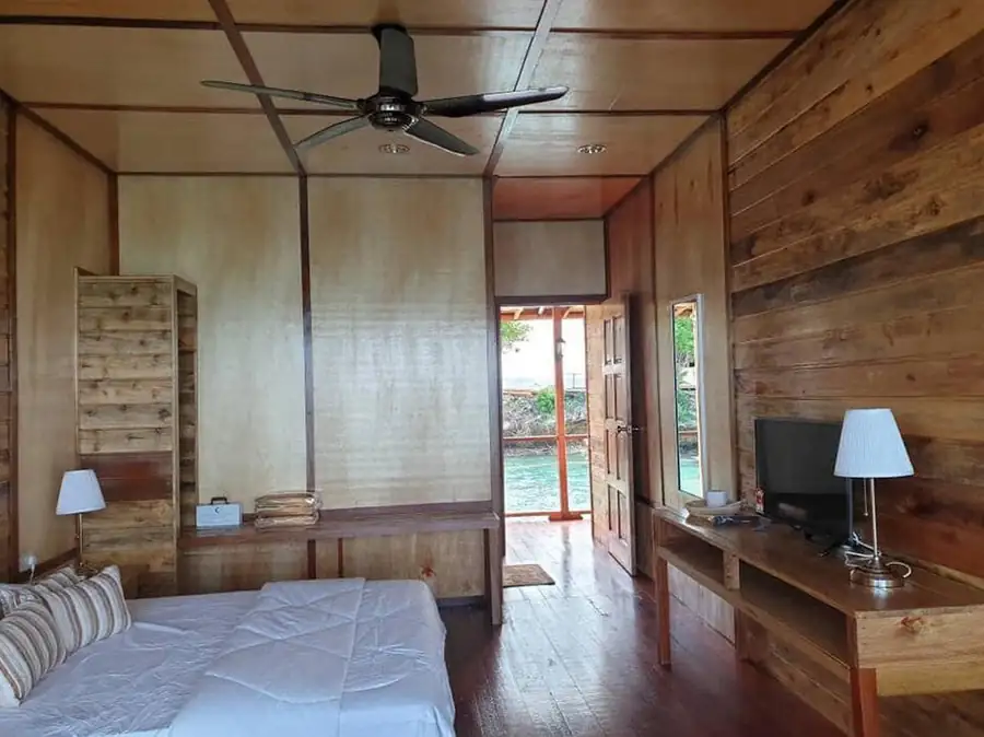 A charming bedroom at Dreamy Wave Dwelling Resort in Semporna featuring a bed facing an open door to the sea, classic timber walls with glossy wooden flooring, and A/C.