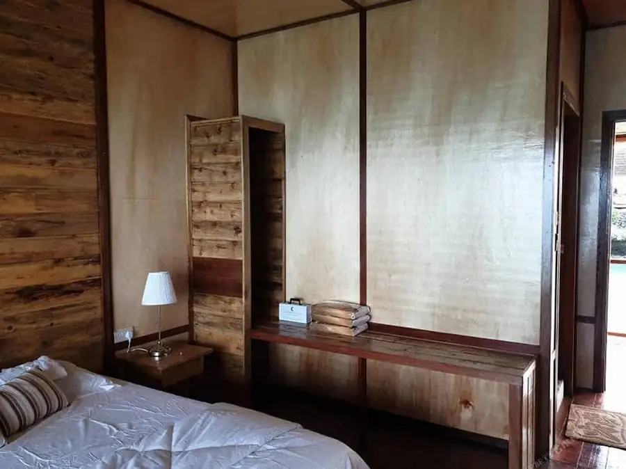 A comfortable bedroom at Dreamy Wave Dwelling Resort featuring a large bed, wooden wardrobe, classic timber walls with glossy wooden flooring, and A/C.