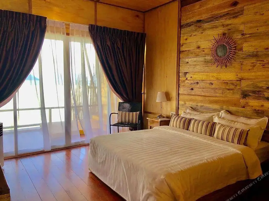 A cozy bedroom at Dreamy Wave Dwelling Resort featuring a large bed, panoramic glass doors framing the seaviews, traditional style wood panel walls with beautiful wooden floors, and AC.